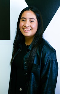 a young woman in a black leather jacket smiling in front of a black and white wall