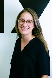a woman in glasses is smiling in front of a black wall